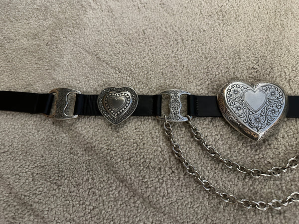 Black belt with heart-shaped metal buckles on a beige carpet